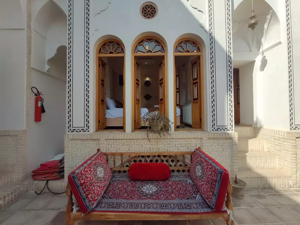 تخت سنتی با فرش و پشتی قرمز در حیاط هتل صباغیان