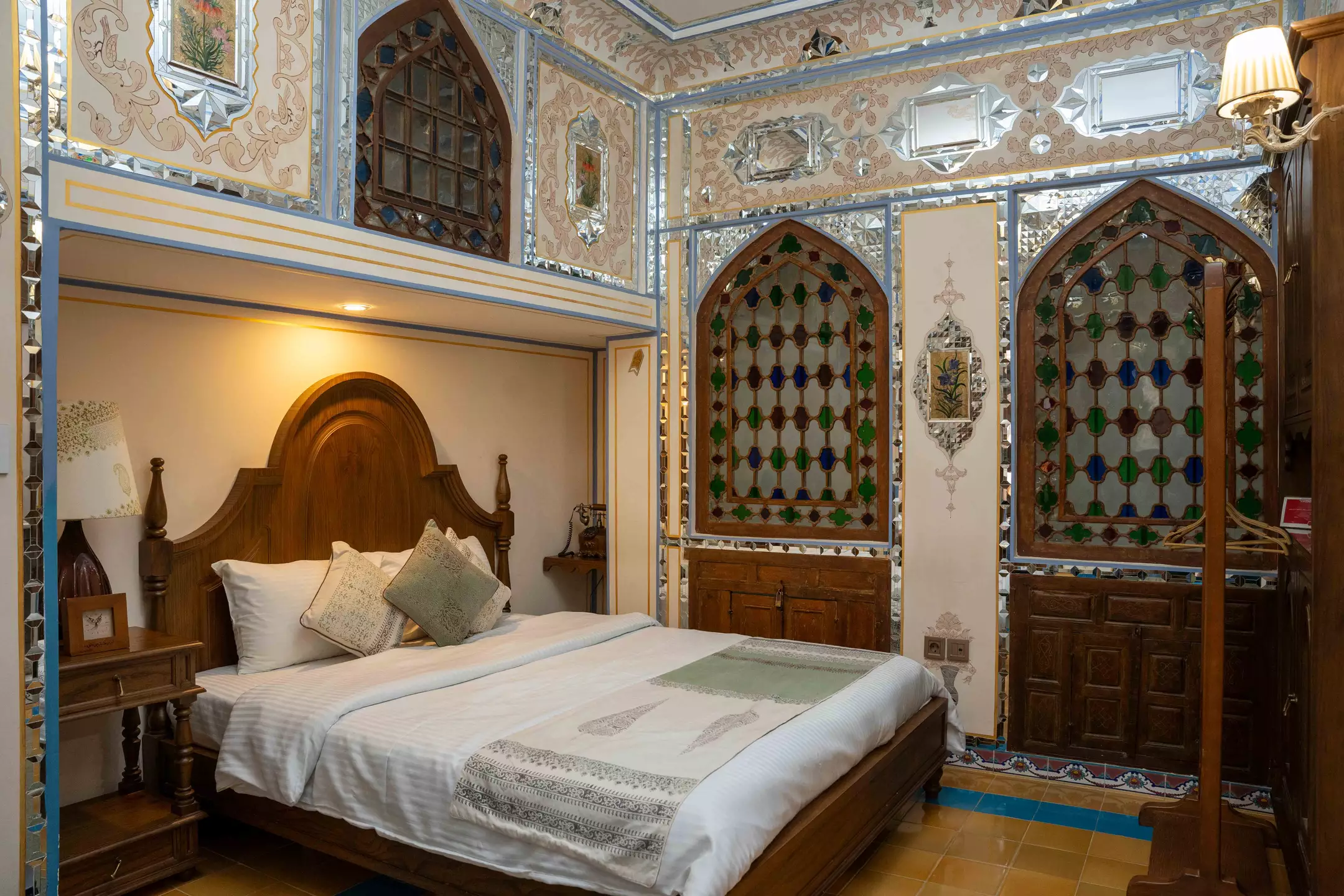 اتاق عمارت شهسواران با تخت چوبی و پنجره‌های رنگی