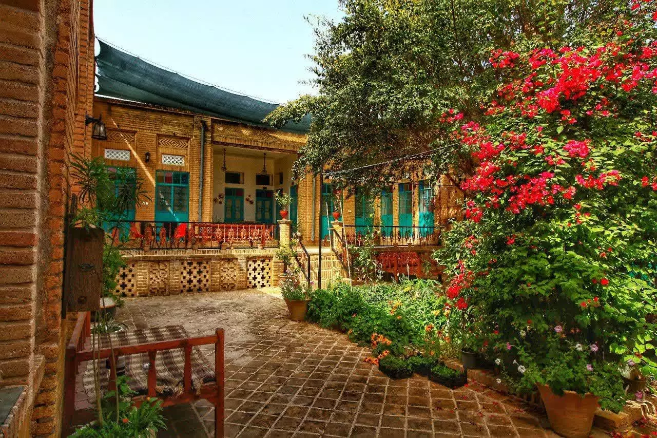 حیاط عمارت پدری با گل‌های سرخ و درختان