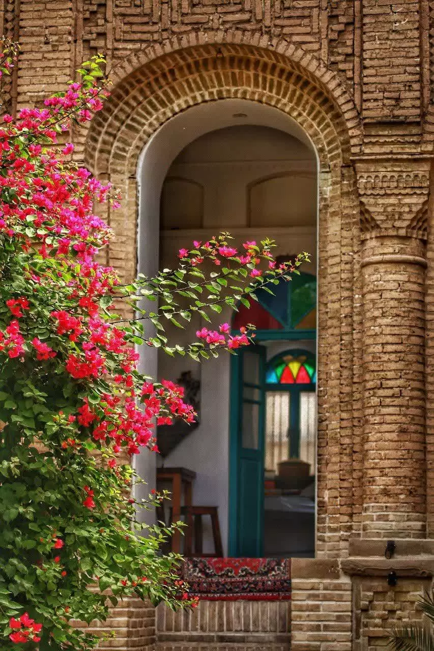 ورودی آجری عمارت پدری در میان گل‌های سرخ