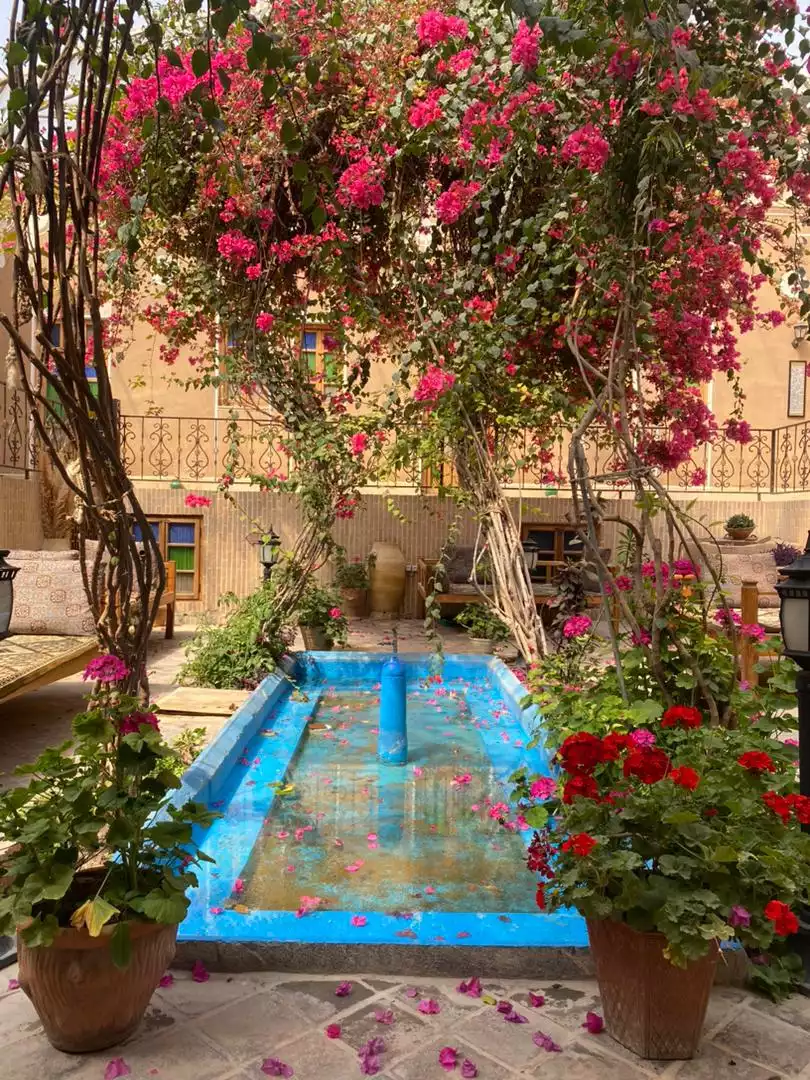 حوض آبی و درختان گل‌دار حیاط سرای کهن
