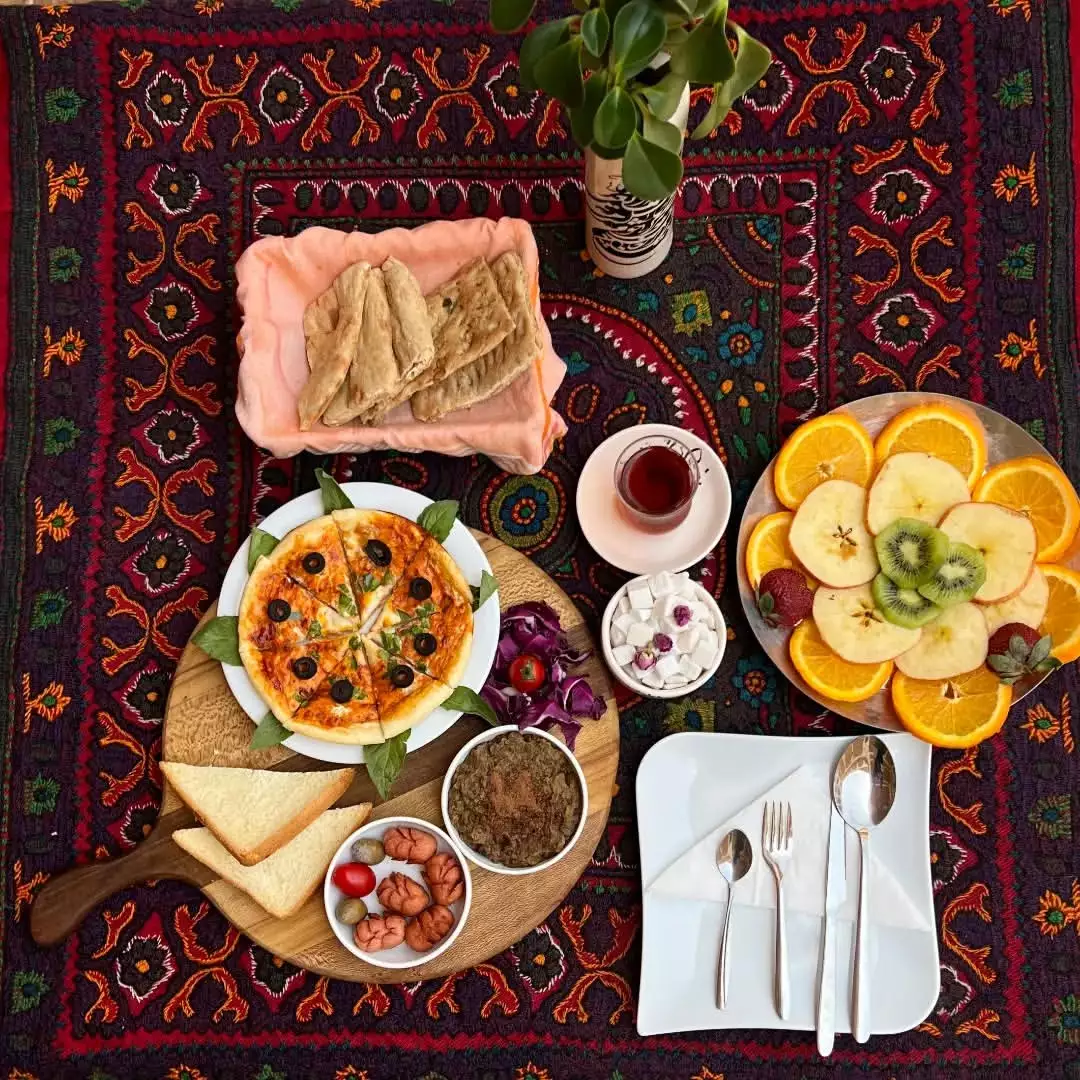چیدمان صبحانه شامل میوه، پیتزا و چای در هتل شیخداد
