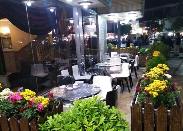 تراس رستوران هتل آریا با میزهای فضای باز و گلدان‌های گل