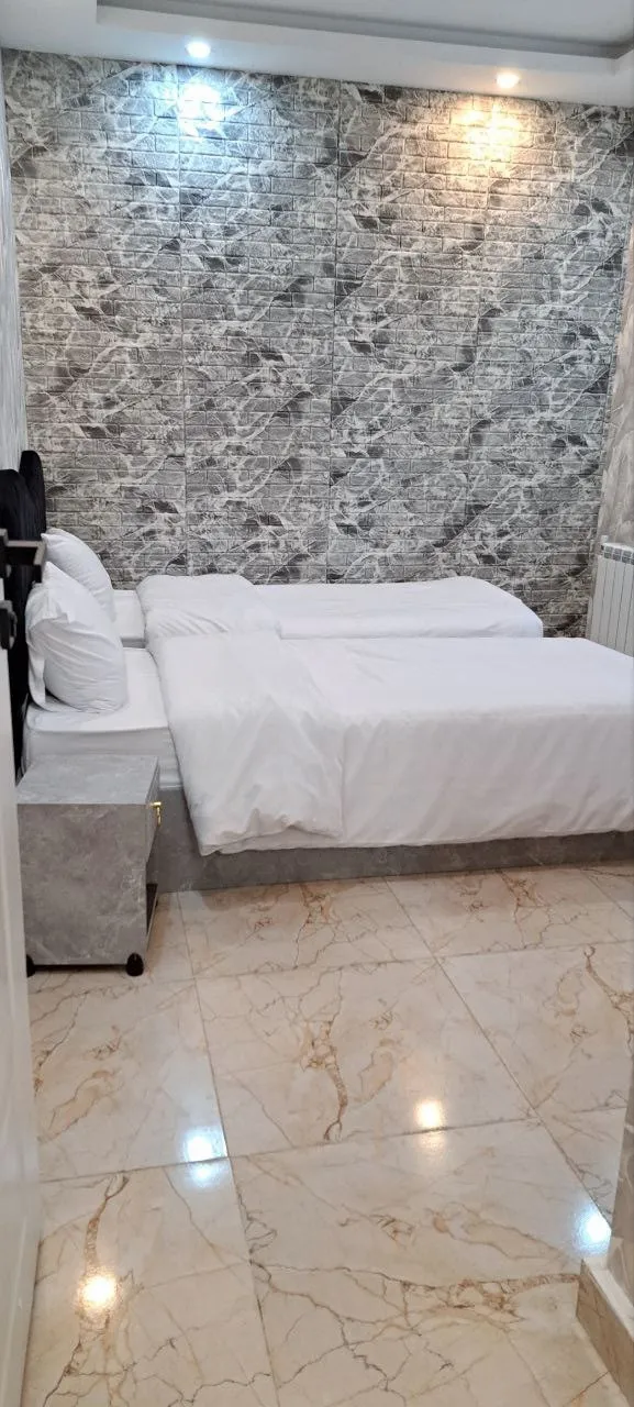 تخت‌های سفید اتاق هتل مازیار با دیوار سنگی