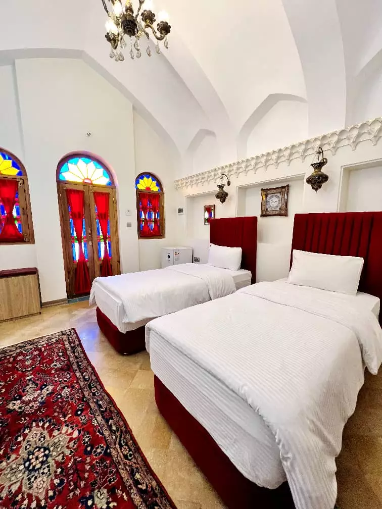 دو تخت یک‌نفره کنار پنجره‌های رنگی عمارت سهروردی