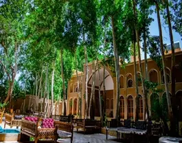 حیاط باغ خوشنویس با درختان بلند و تختهای سنتی
