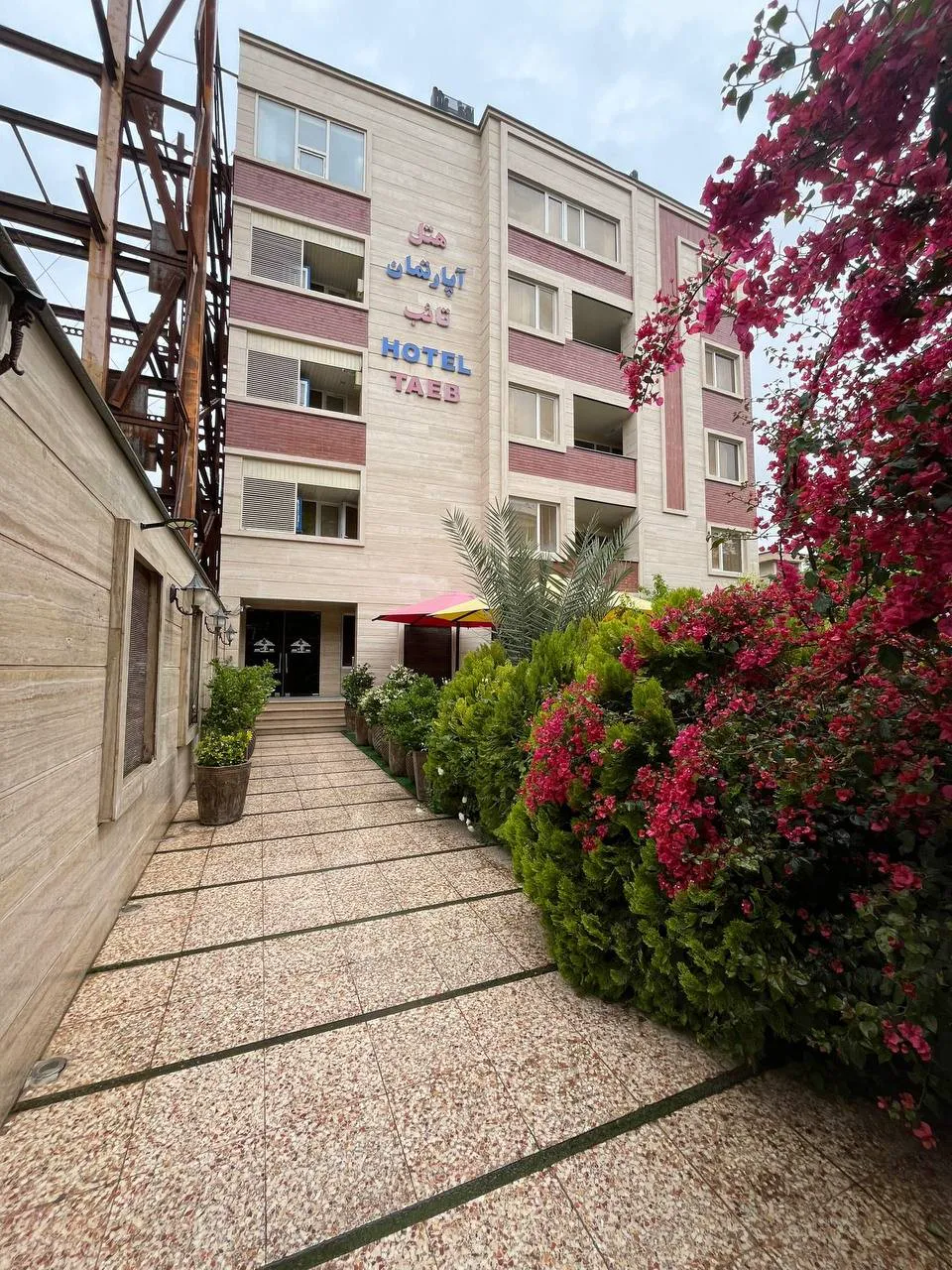 نمای بیرونی هتل تائب در میان درختان و گل‌ها
