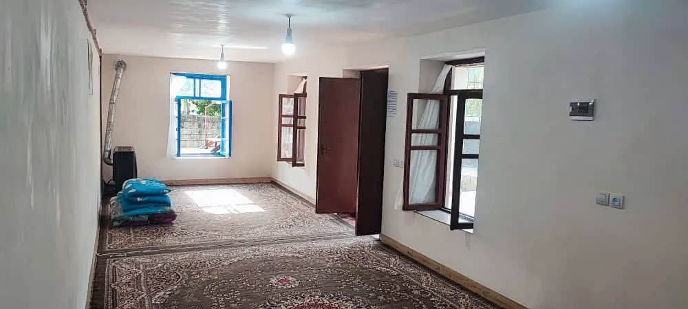 اتاق ساده با فرش ایرانی و پنجره‌های چوبی در اکبربابا