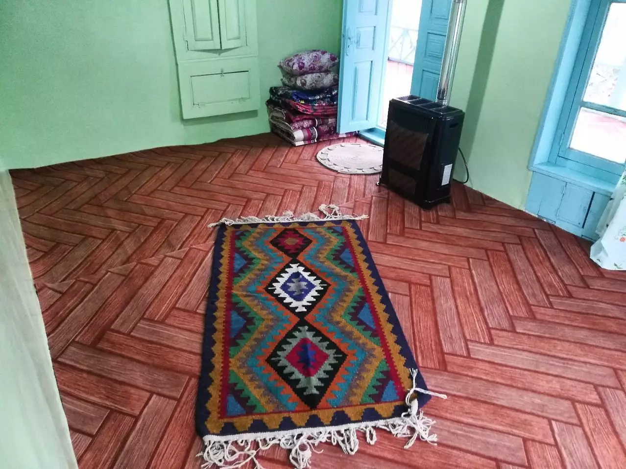 اتاق اقامتگاه حاج حسین پرویزی با قالیچه رنگارنگ و کفپوش چوبی