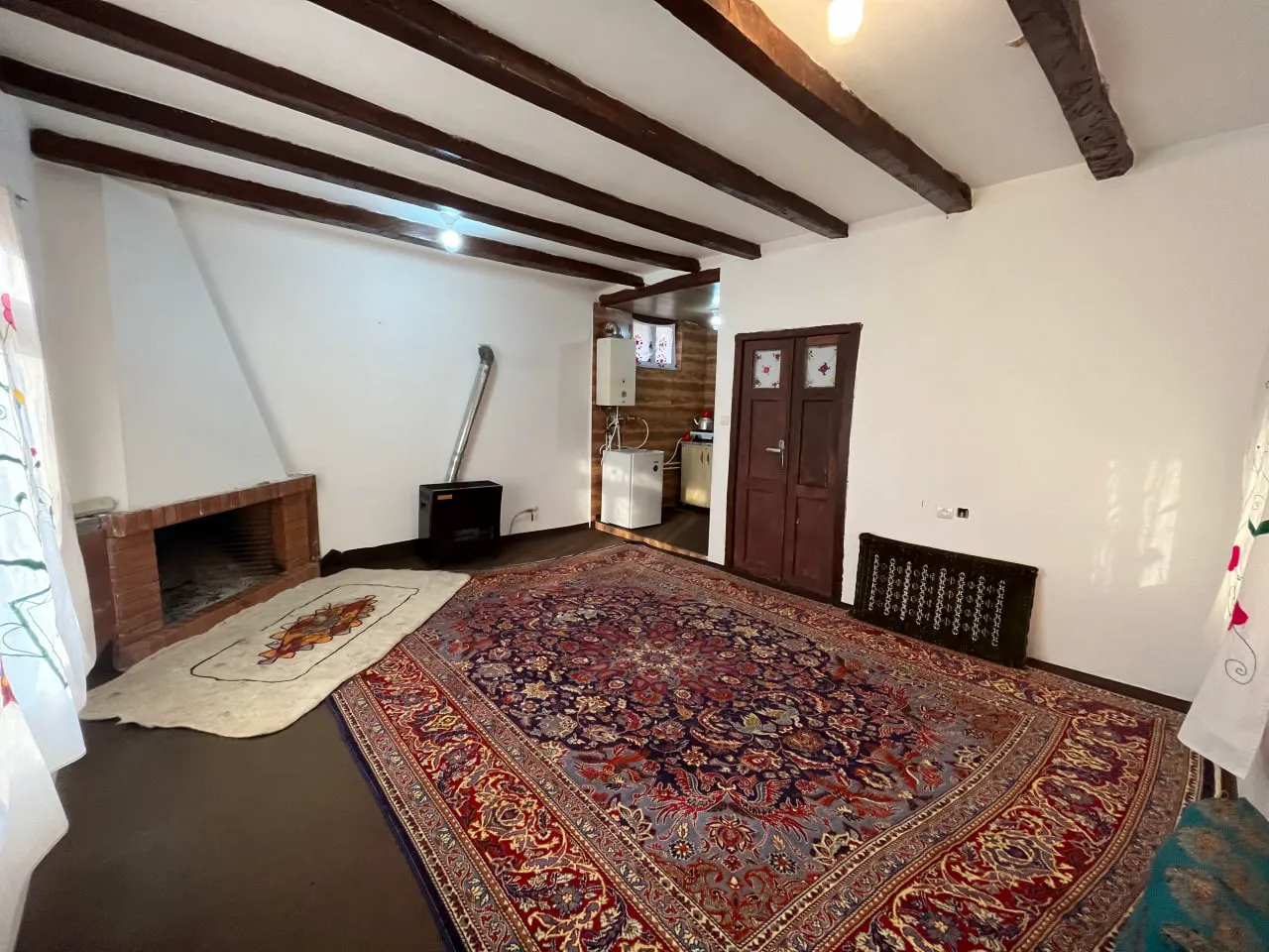 اتاق اقامتگاه نماشان با قالیچه بزرگ و بخاری دیواری