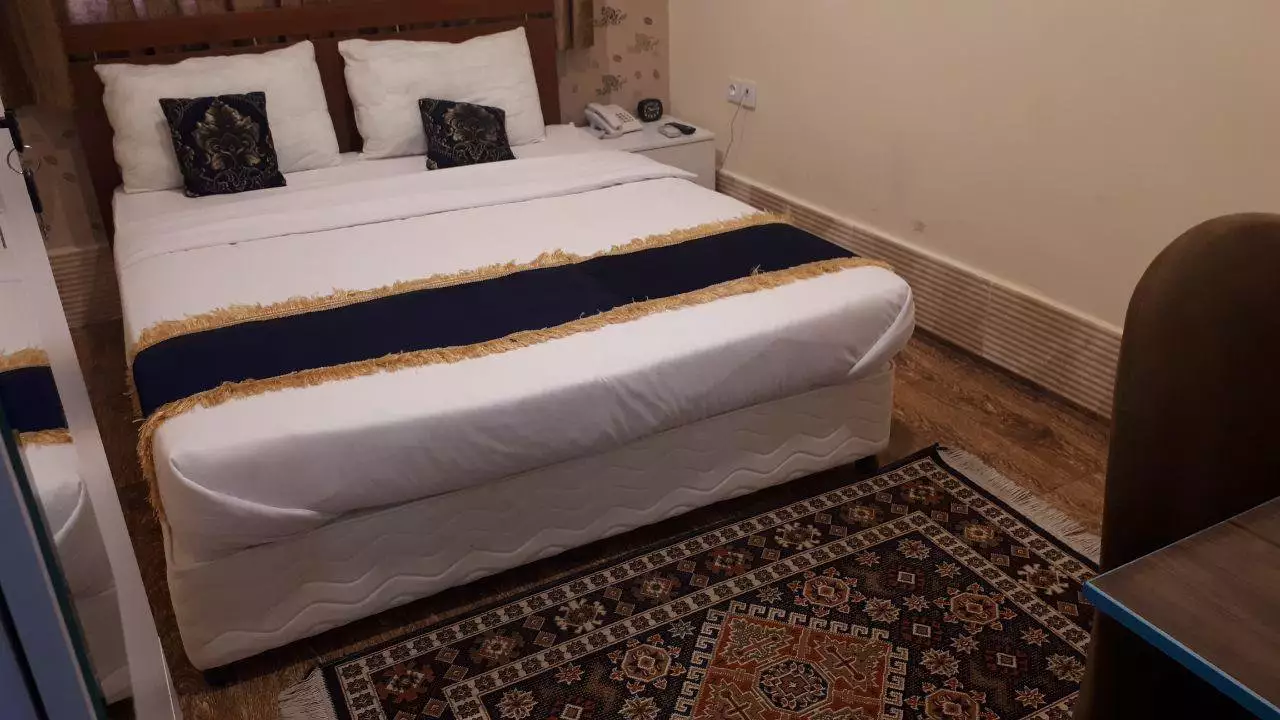 تخت دونفره سفید با روتختی سرمهای در هتل آکراس