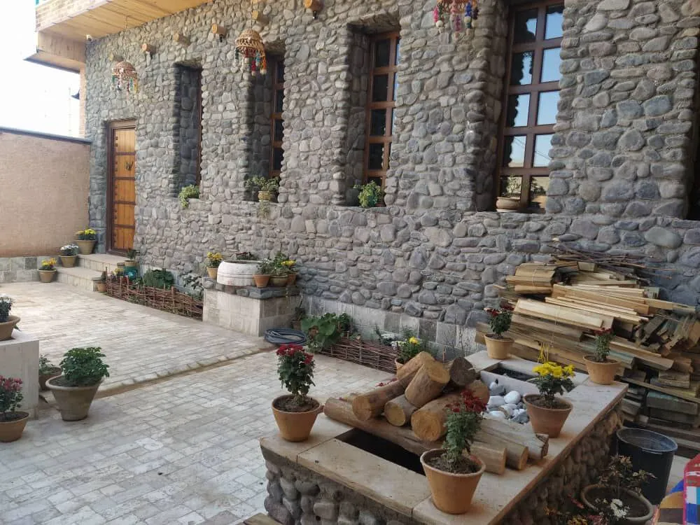 حیاط سنگ‌چین اقامتگاه گلجان با گلدان‌های رنگارنگ
