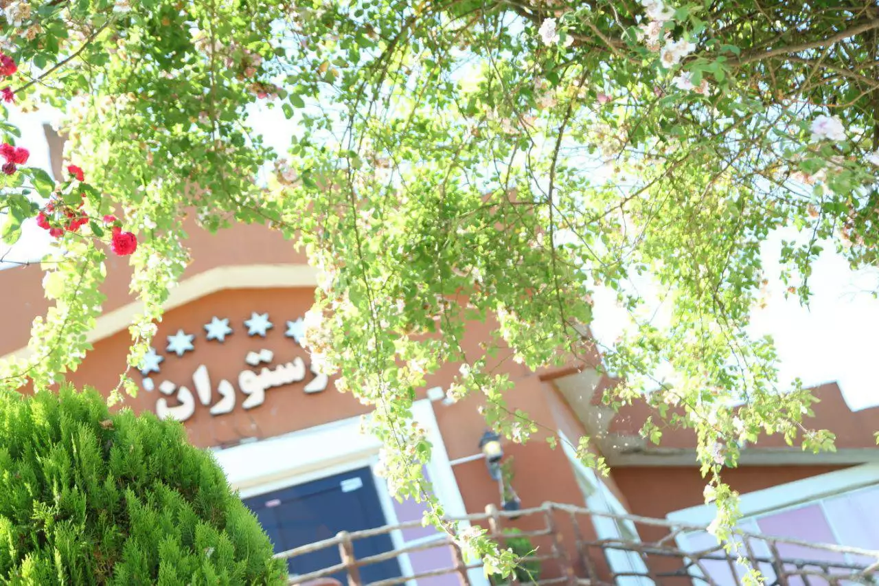 نمای رستوران مهرگان پشت درختان و گل‌های آویخته