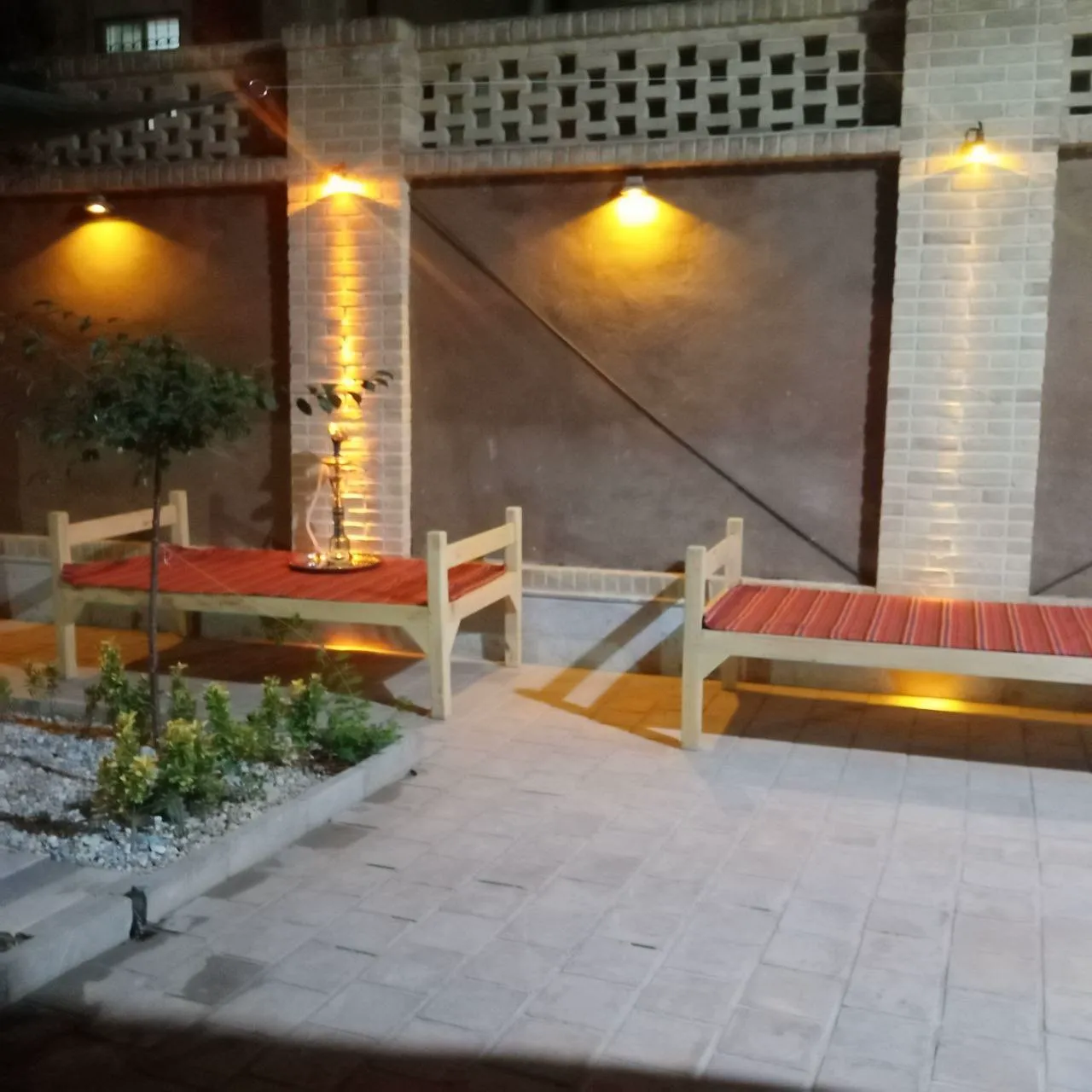 تخت‌های چوبی با تشک قرمز در حیاط هشت بهشت