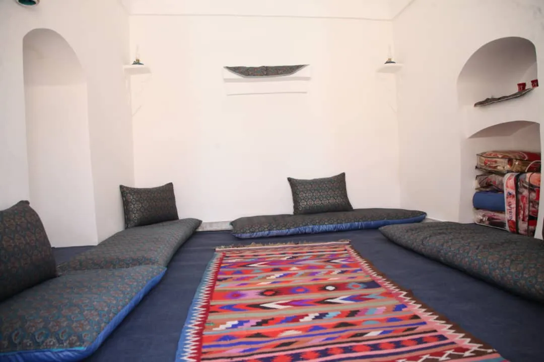 اتاق نشیمن خانه خشتی با پشتی‌های سنتی و قالی رنگارنگ