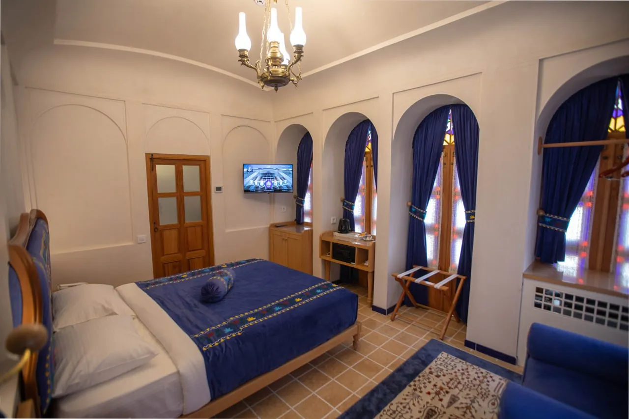 اتاق خواب عمارت آقاحسینی با تخت آبی و پنجرههای قوسی
