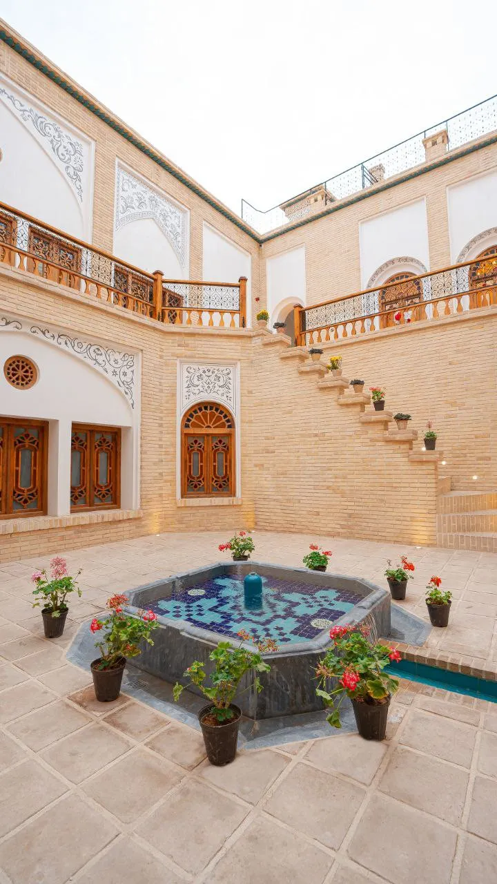 حوض کاشی‌کاری‌شده در حیاط هتل ایوان با گلدان‌های گل