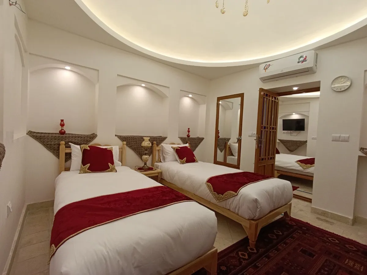 دو تخت یک‌نفره و آینه قدی در اتاق عمارت شمسه