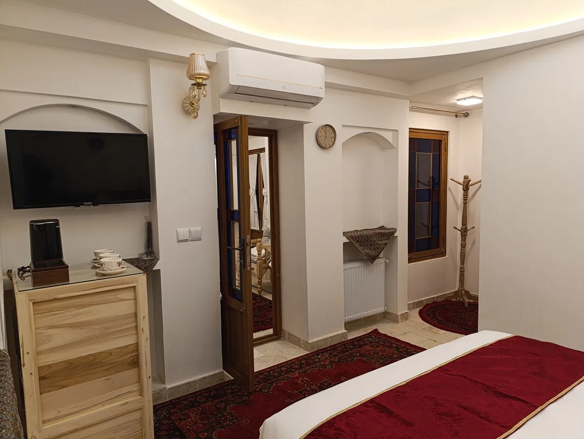 تلویزیون دیواری و تخت با روتختی زرشکی در عمارت شمسه