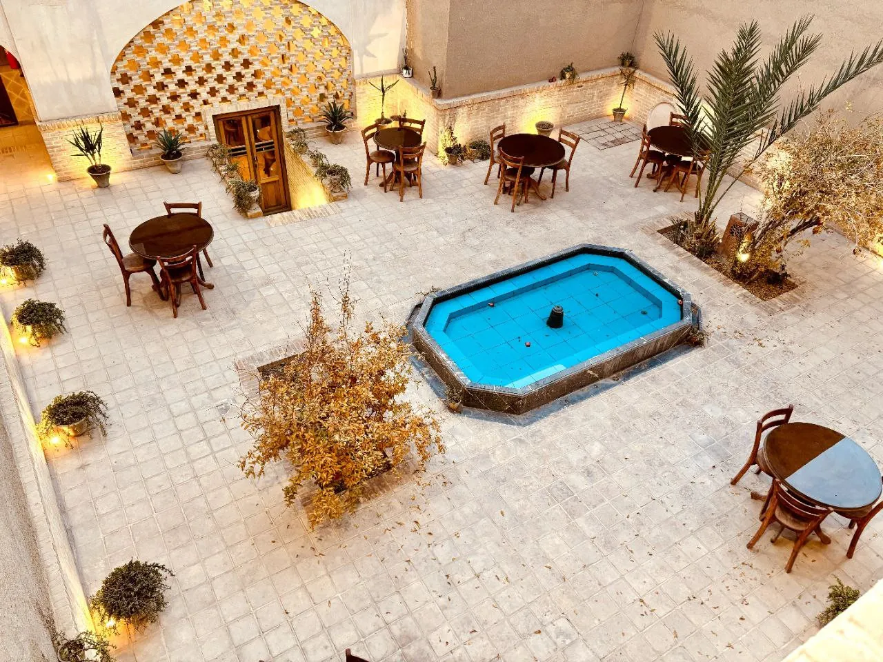 حیاط سرای طاق چشمه با حوض آبی و میزهای چوبی