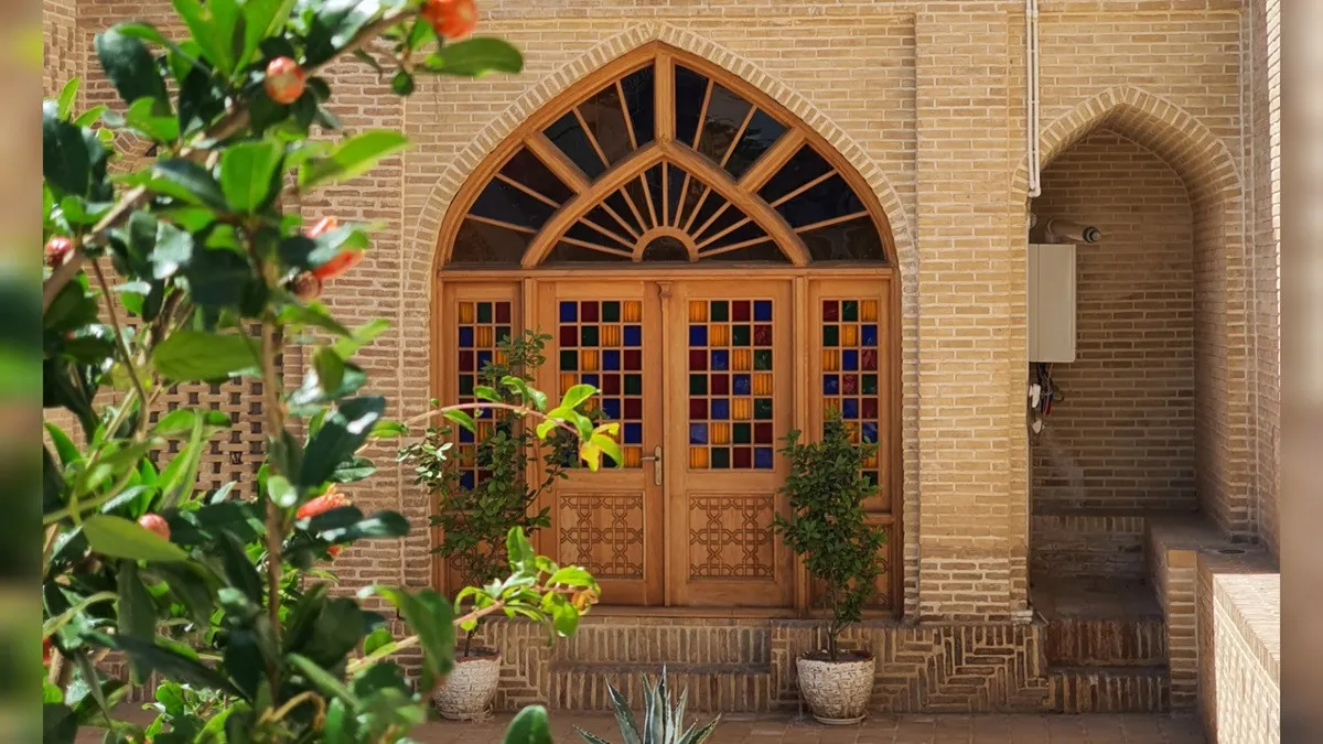 در چوبی قوس‌دار و گلدان‌های ورودی عمارت حاکم