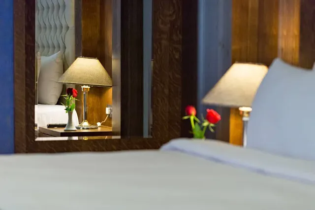 تخت هتل هما با چراغ خواب و گلهای رز