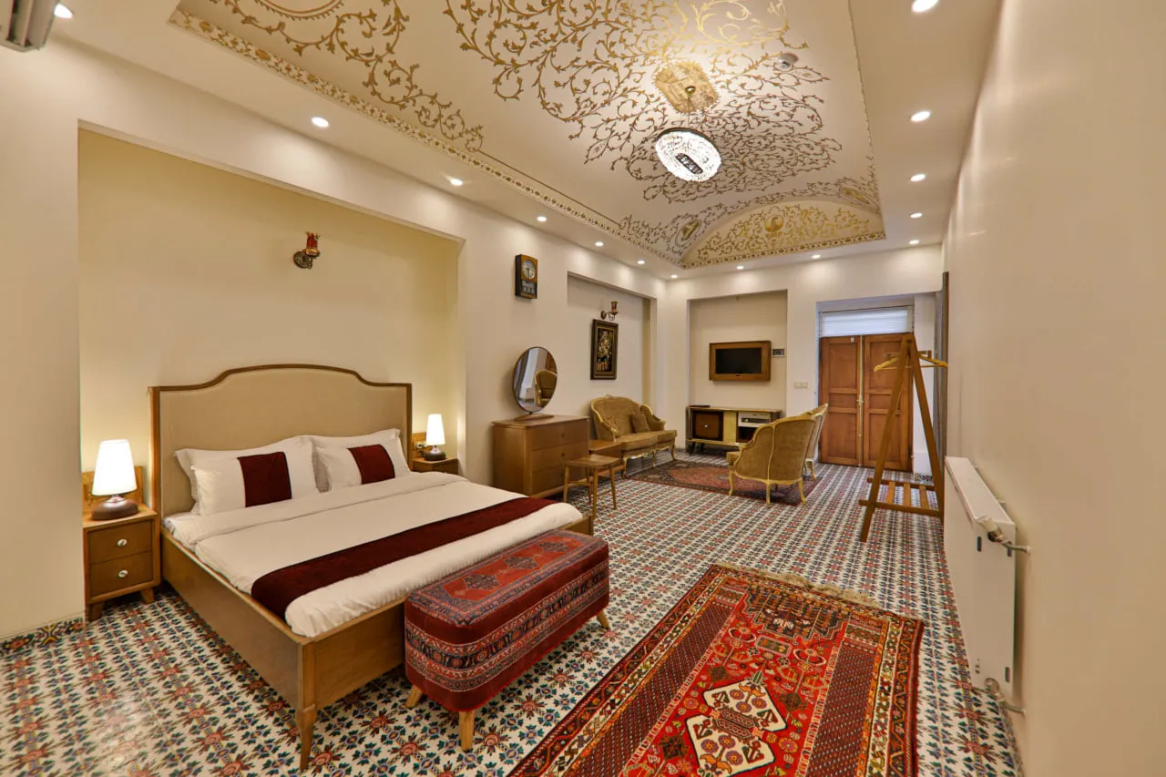 اتاق خواب عمارت فرهادی با فرش‌های ایرانی و سقف گچ‌بری‌شده