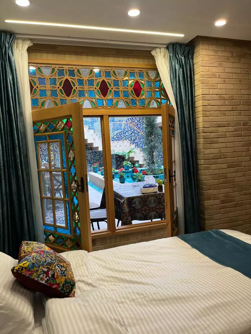 تخت اتاق با پنجره شیشه‌رنگی هتل ماه گیسو