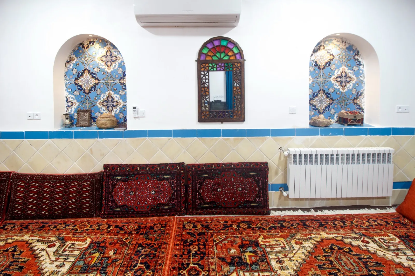 اتاق نشیمن سرای امیر بیک با فرش‌های ایرانی و پنجره رنگی