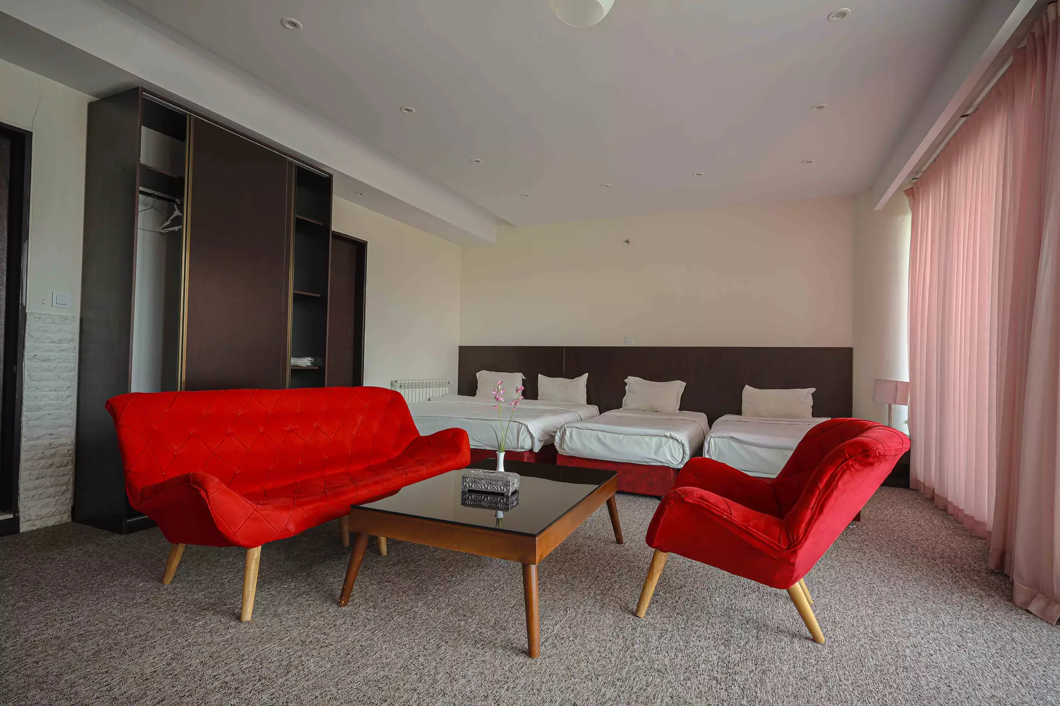 اتاق هتل کیمیا با تخت‌های یک‌نفره و مبل قرمز