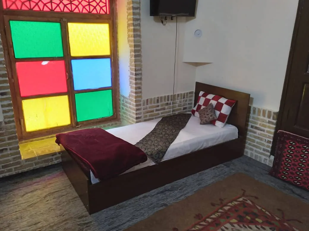 تخت یک‌نفره کنار پنجره رنگی عمارت خورشید پردیسان