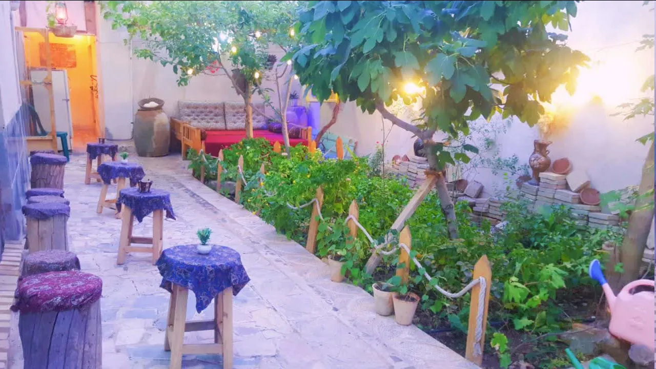 حیاط سرسبز اقامتگاه خاطره با میزهای کوچک