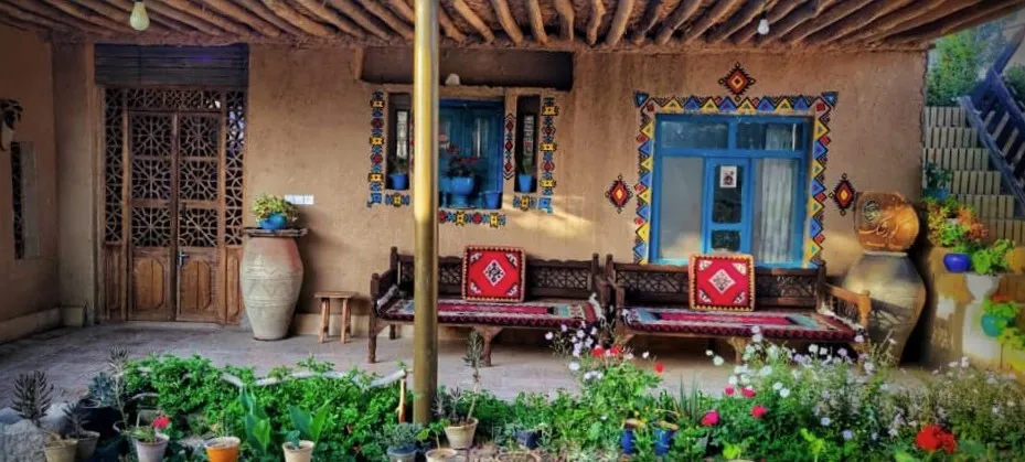 ایوان خانه کورشک با پنجره آبی و باغچه گلدار