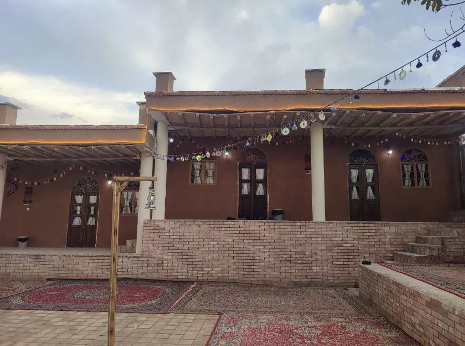 حیاط سنتی اقامتگاه دزپارت اردل با فرش و ریسه‌های رنگی