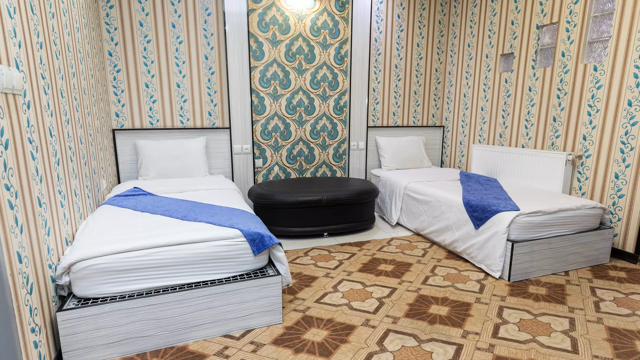 دو تخت یک‌نفره با روتختی آبی در هتل بوستان