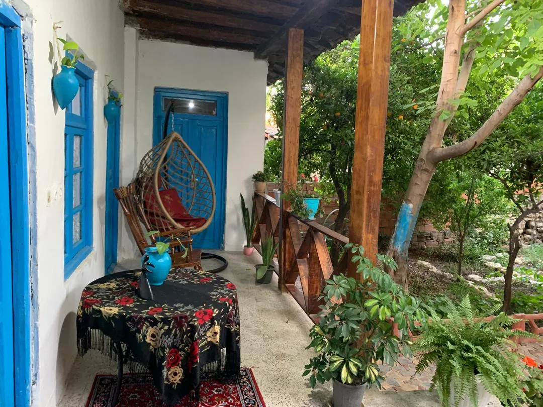 ایوان خانه بابا بزرگ با تاب حصیری و میز گل‌دار