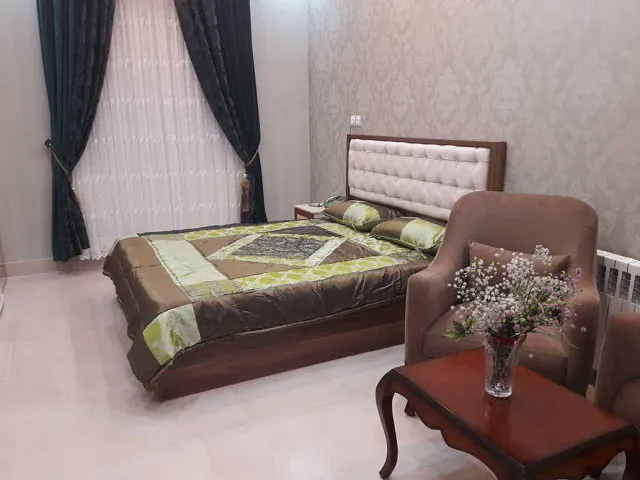 تخت دونفره و صندلی گل‌دار اتاق هتل پارمیس