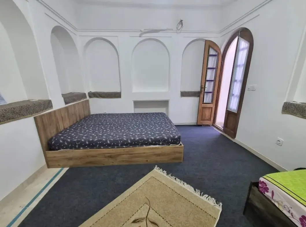 اتاق اقامتگاه خانه خاتون با تخت چوبی و پنجره قوسی