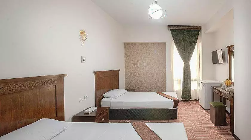 دو تخت چوبی و پنجره پرده‌دار در اتاق هتل رضویه