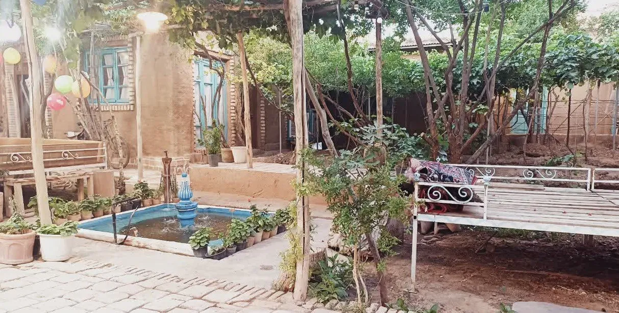 حیاط سرسبز اقامتگاه گلک بانو با حوض و تخت چوبی
