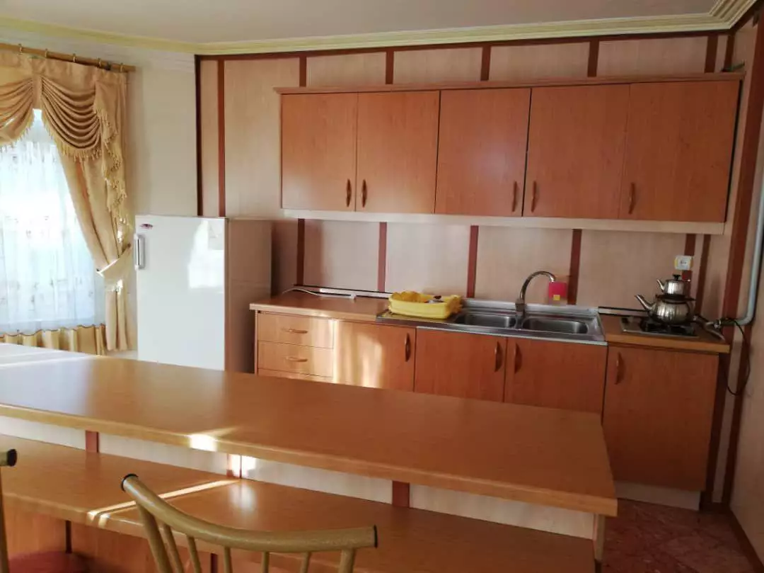 آشپزخانه با کابینت چوبی، یخچال و میز غذاخوری در تخت جمشید