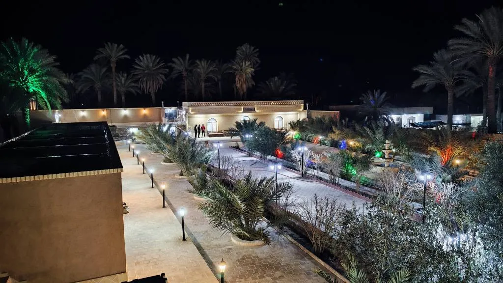 محوطه هتل آقامیرزا با نخل‌ها و مسیرهای روشن در شب