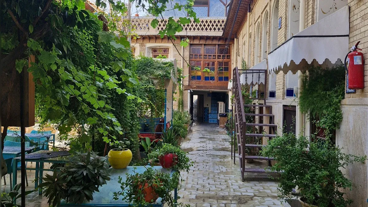 حیاط سرسبز و سنگ‌فرش‌شده هتل سنتی نیایش
