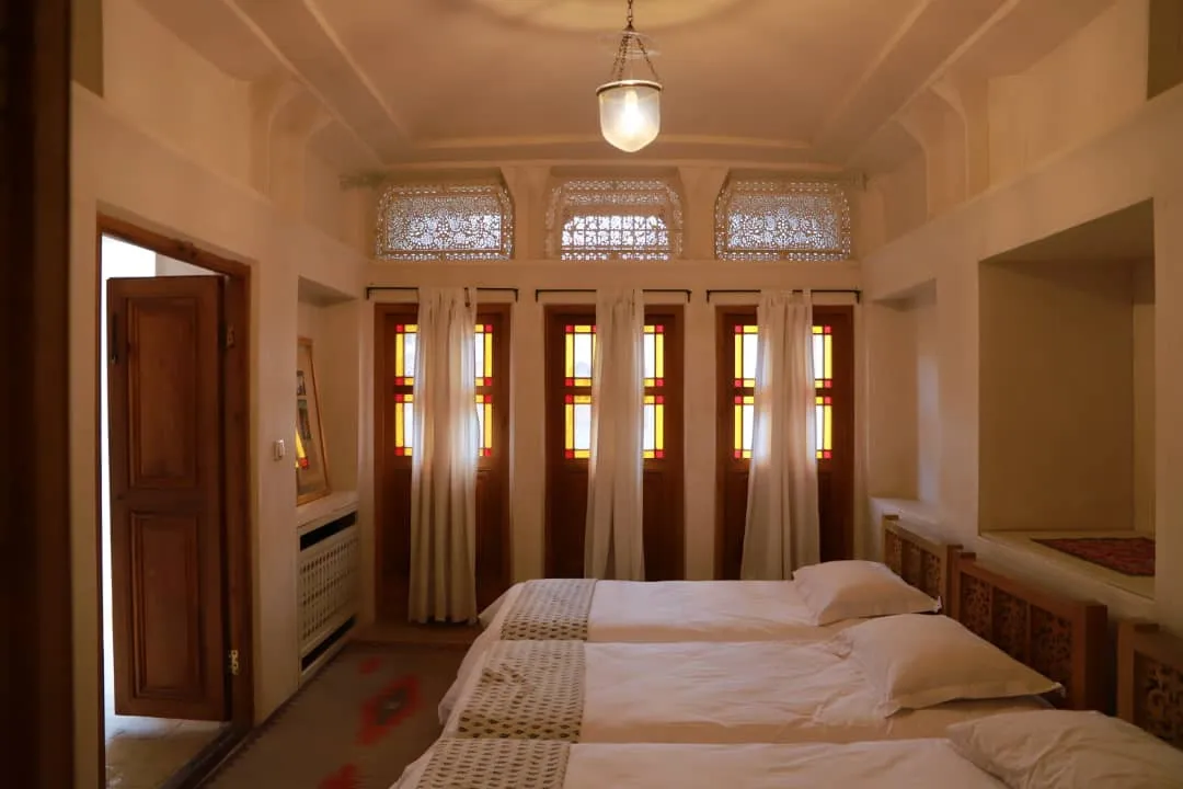 اتاق منوچهری با پنجره‌های شیشه‌رنگی و تخت‌های سفید