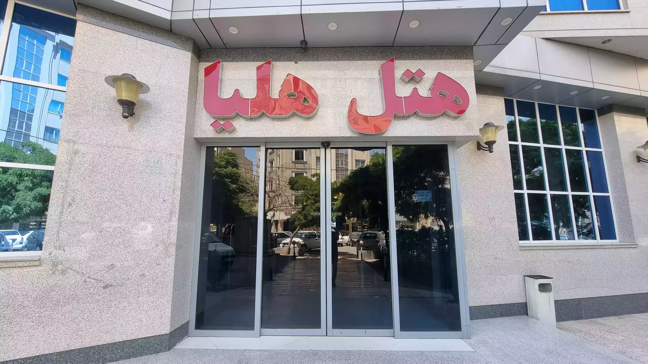 ورودی شیشهای هتل هلیا با تابلوی قرمز