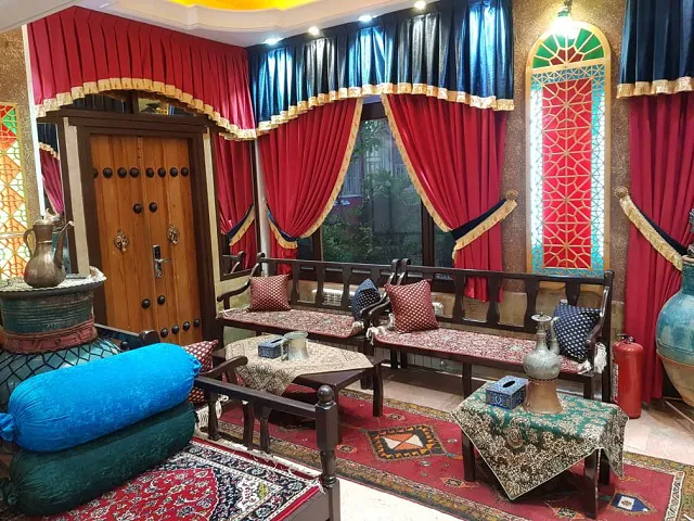 نشیمن سنتی هتل ابیانه با فرش‌های ایرانی و پرده‌های سرخ
