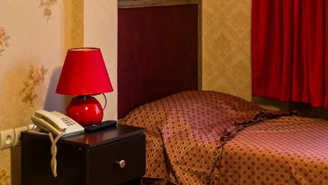 تخت اتاق هتل رازی کنار چراغ رومیزی قرمز و تلفن