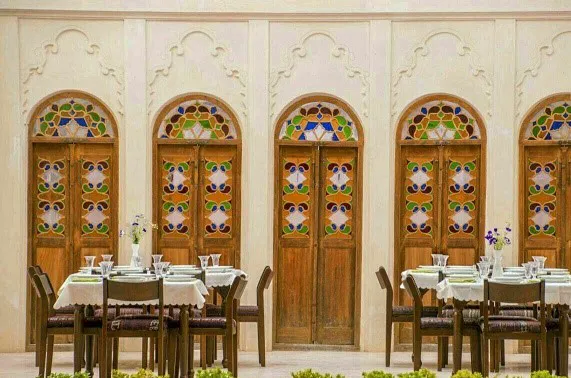 میزهای غذاخوری مقابل درهای چوبی رنگین تاریخی خانه آقازاده