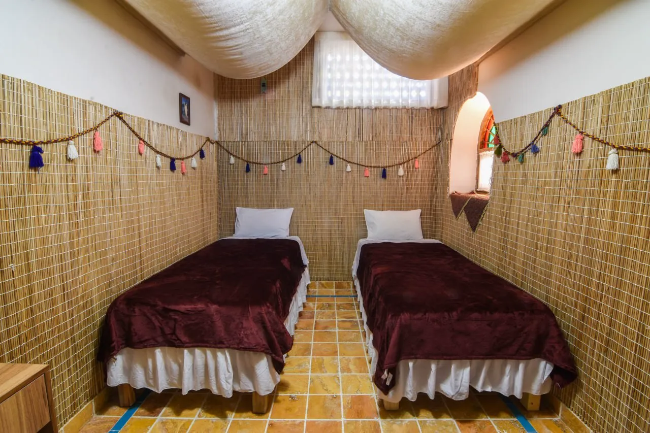 دو تخت یک‌نفره با روتختی مخمل زرشکی در سرای ملک