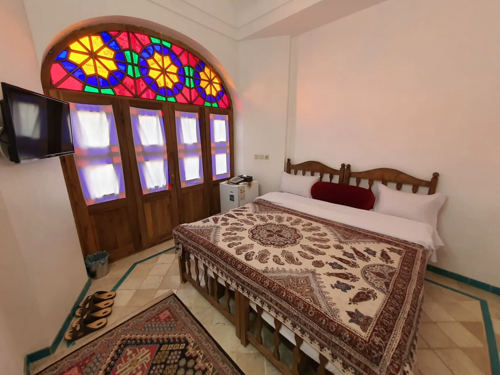 اتاق خواب هتل اطلسی با پنجره شیشه‌رنگی و تخت فرش‌شده